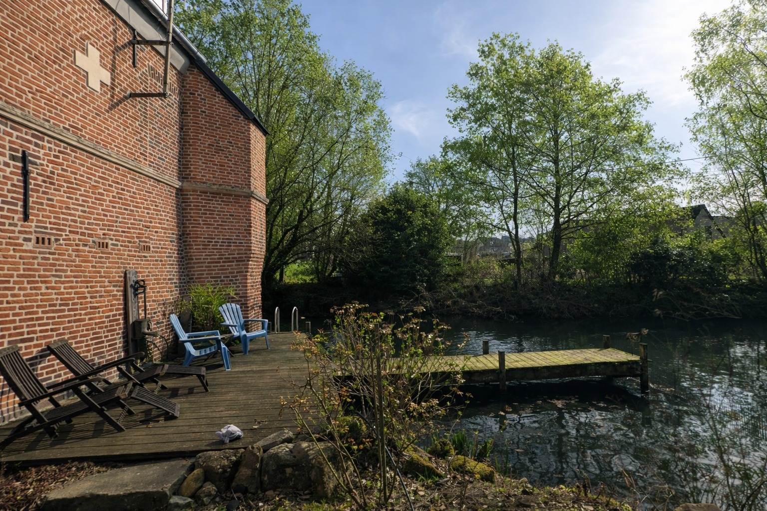 Terrasse en bois au bord de l'eau avec ponton et chaises, espace de repos du Moulin des Passages